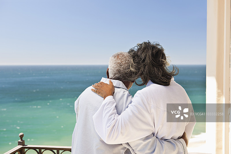 年长夫妇身穿浴袍在阳台上拥抱，眺望大海图片素材