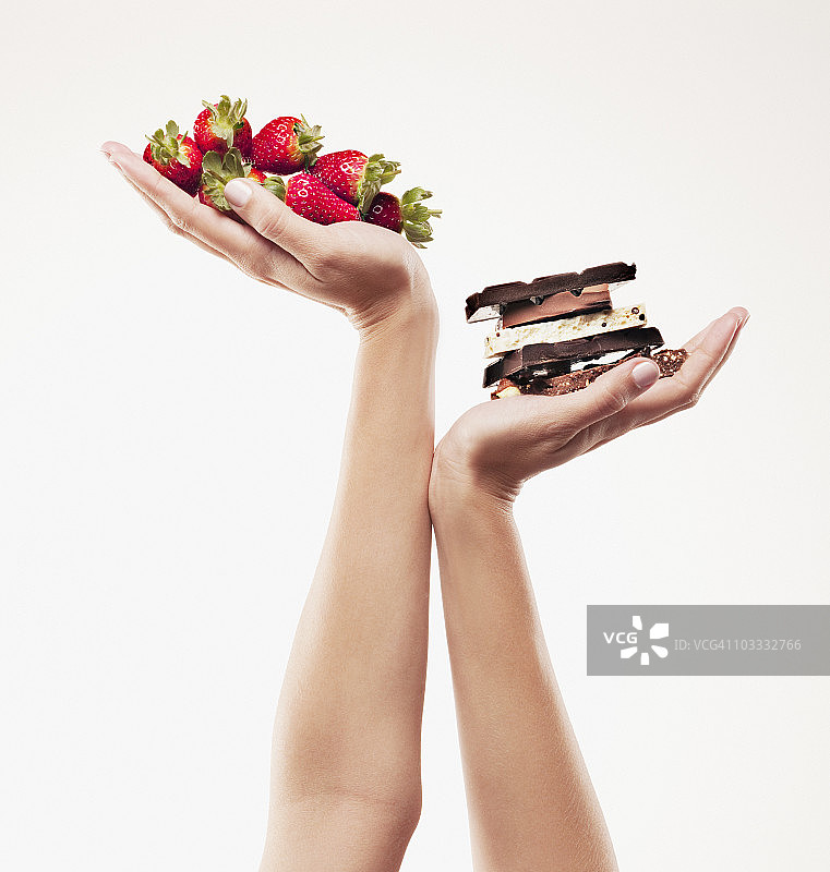 女人拿着草莓放在巧克力棒上方图片素材