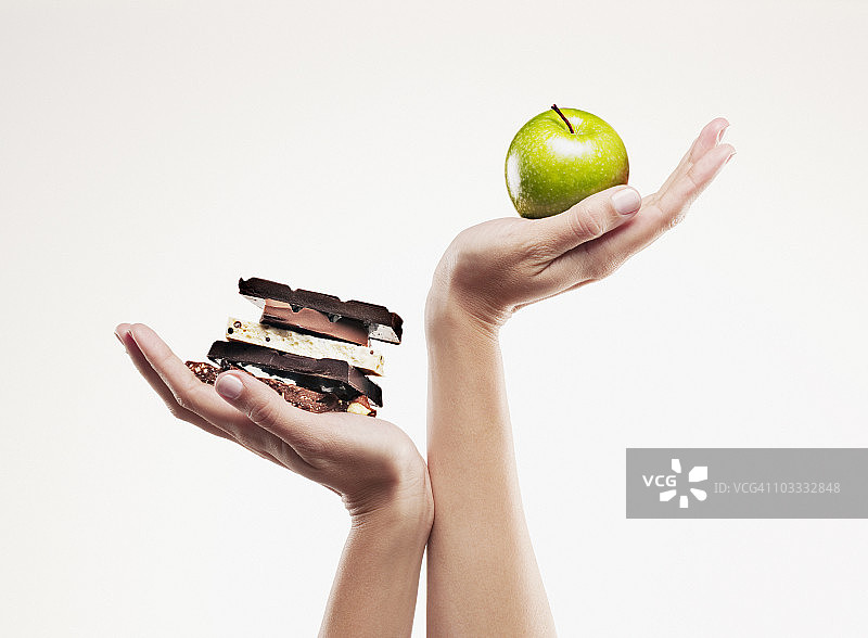 女人手捧绿色苹果置于巧克力棒上方图片素材