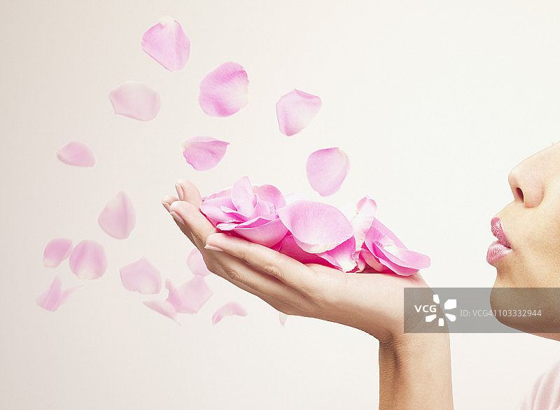 吹粉色玫瑰花瓣的女人图片素材