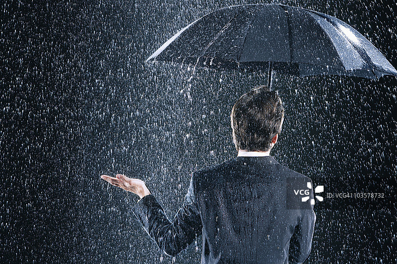 暴雨中，商人撑伞保持干燥，背影图片素材