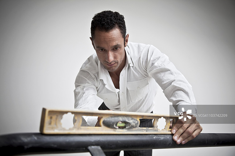 西班牙裔男子在栏杆上使用水平仪图片素材