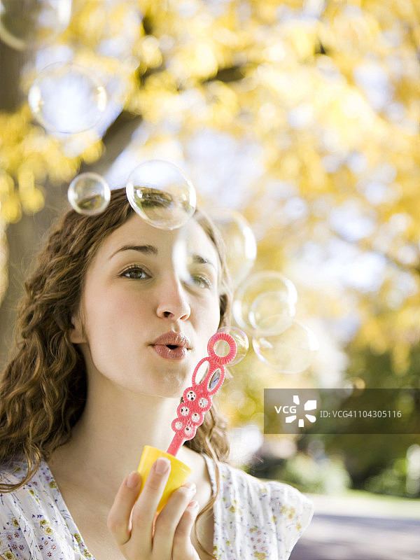 在秋日森林里吹肥皂泡泡的年轻女子图片素材