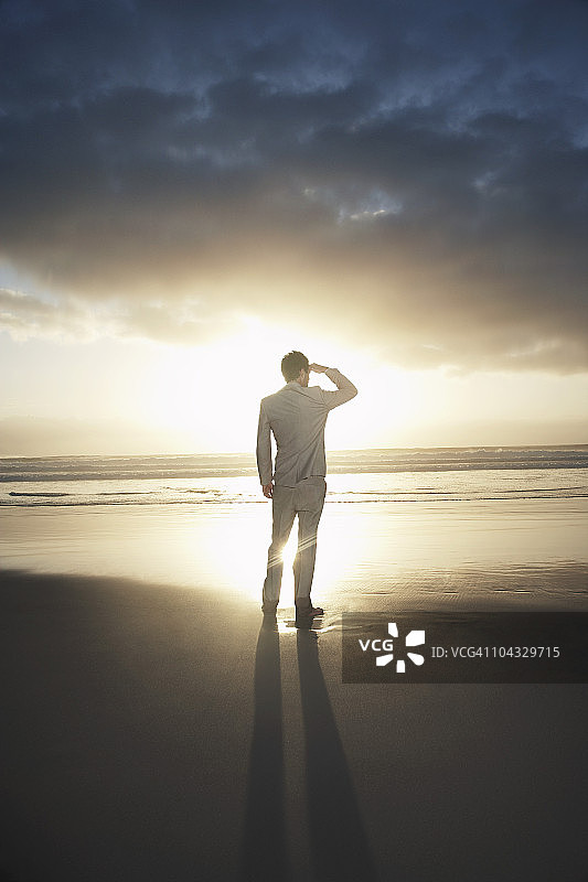 站在海滩上、日落时分眺望地平线的商人背影图片素材