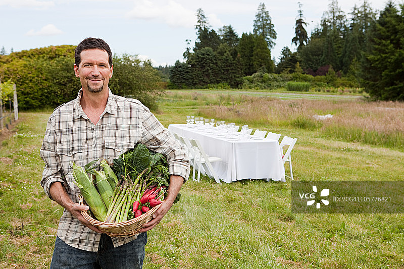 在田野里拿着一篮子农产品，背景是桌子的男人图片素材