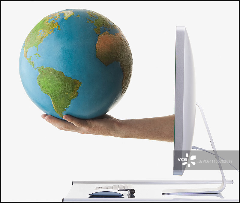 从电脑屏幕伸出的手臂上的地球仪图片素材