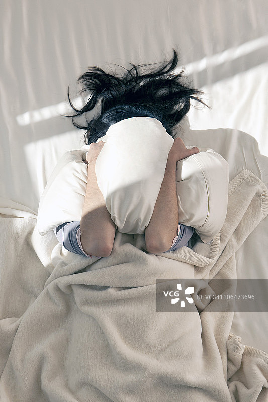 女子用枕头遮挡清晨的阳光图片素材