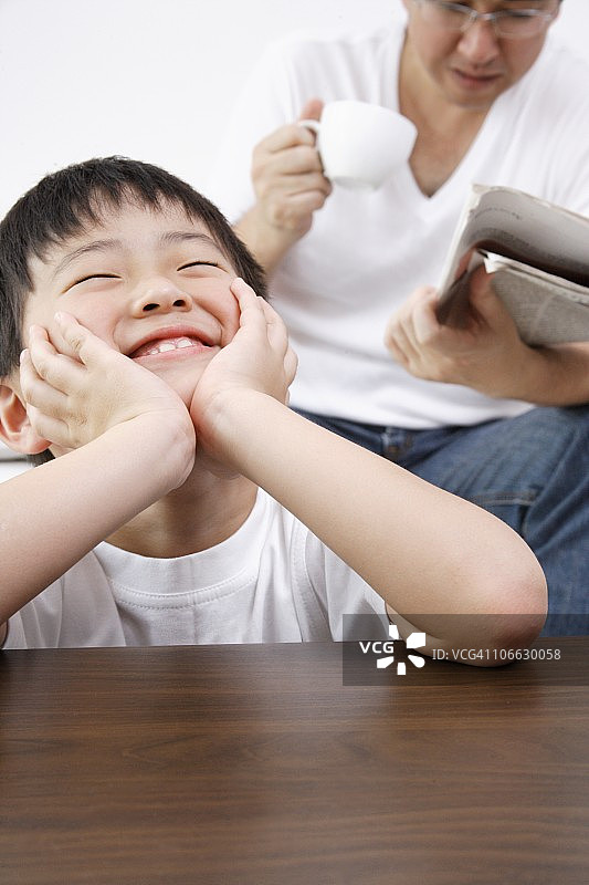 男孩和正在读报纸的父亲一起做白日梦图片素材