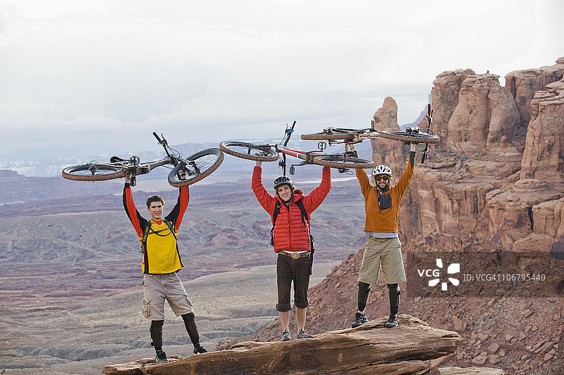 三位年轻男子在犹他州摩押的Amasa Back Trail上举着自行车图片素材