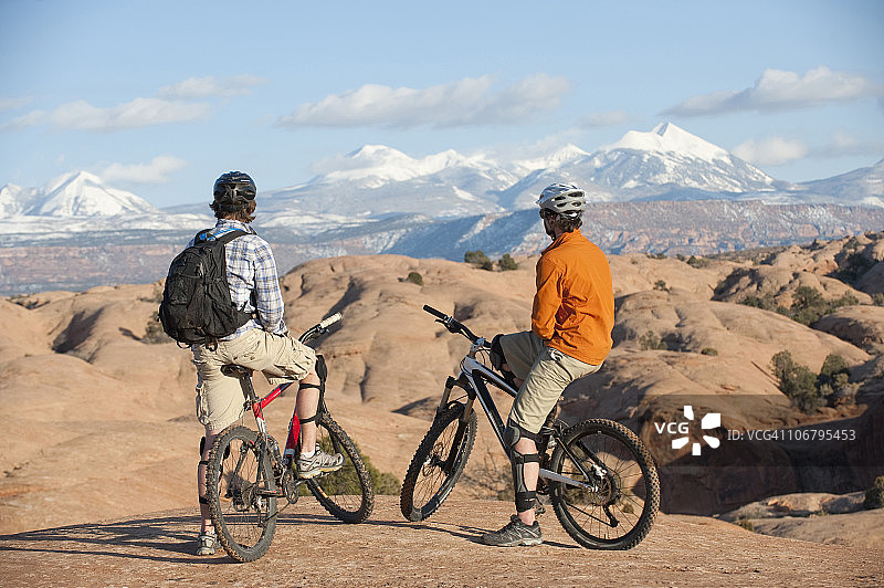 两名年轻男子在犹他州莫阿布的斯利克罗克小径上骑山地自行车欣赏风景图片素材