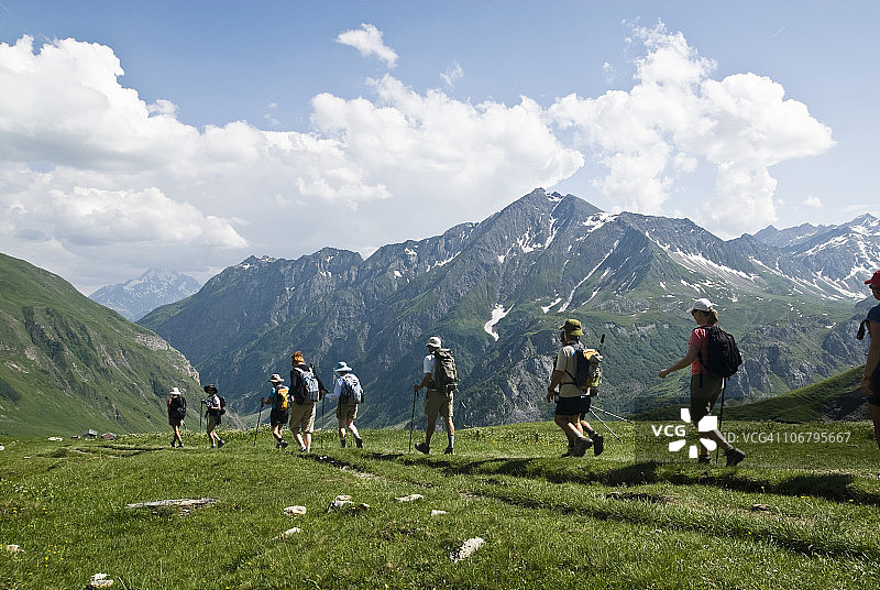 在部分多云的天气里，一群徒步旅行者在法国霞慕尼上方的一片绿色山坡上跋涉图片素材