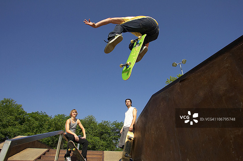 三位滑板运动员在滑板公园表演技巧图片素材