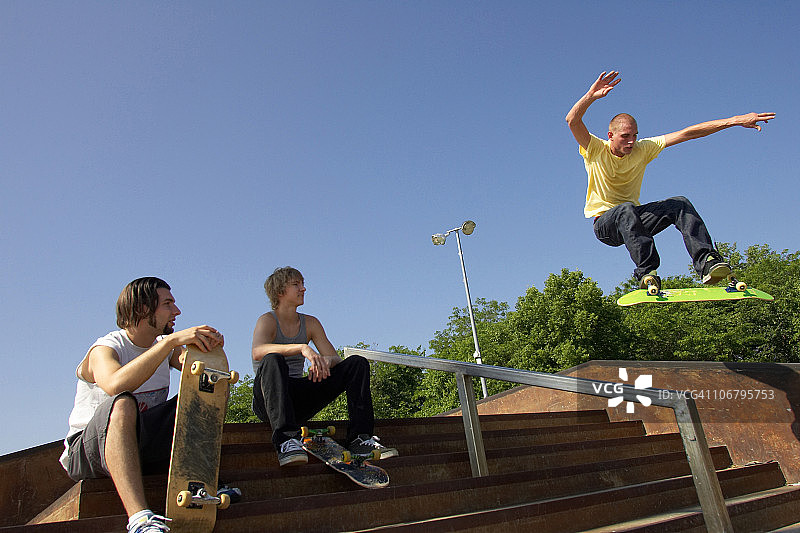 三位滑板运动员在滑板公园表演技巧图片素材
