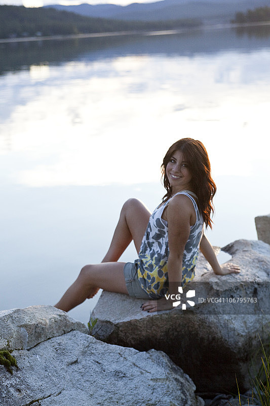 年轻女人在日落时坐在湖边微笑图片素材