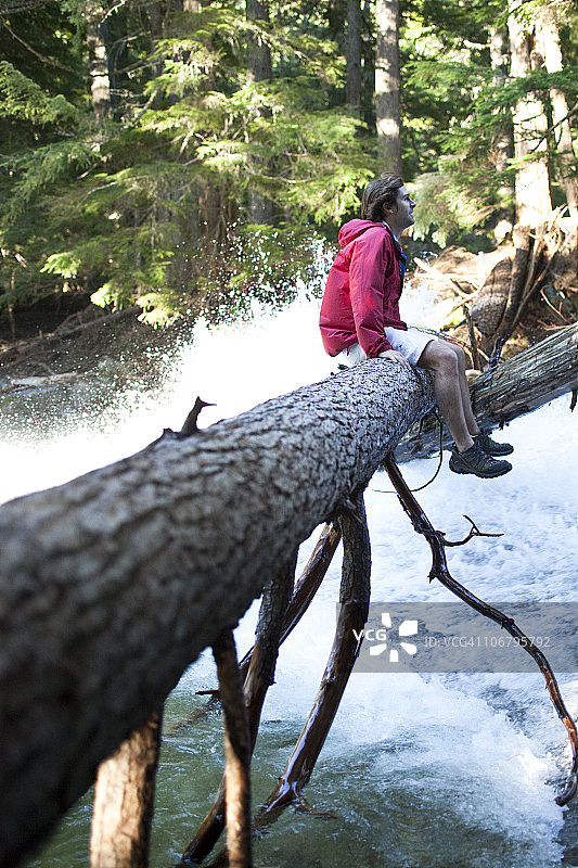年轻男人坐在爱达荷州瀑布上的原木上图片素材