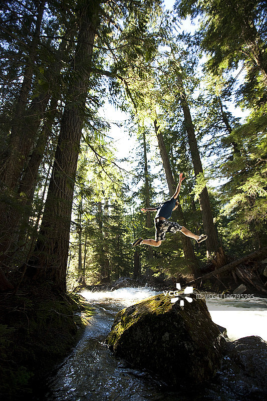 在森林里，年轻人跳下河边的岩石图片素材