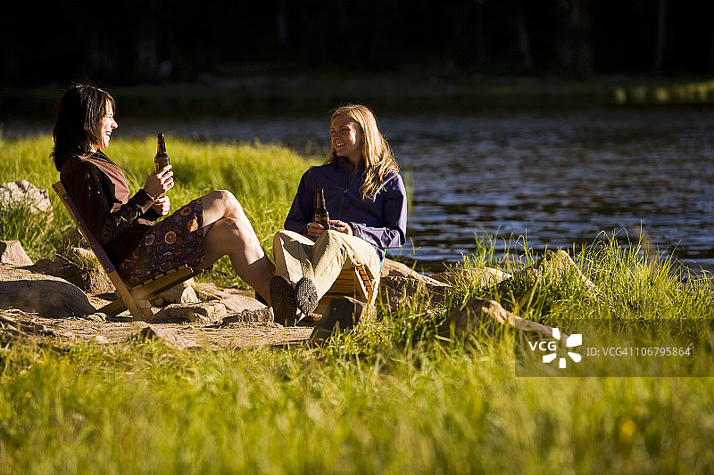 两个女人在山间湖岸边一边欣赏美景一边喝啤酒图片素材