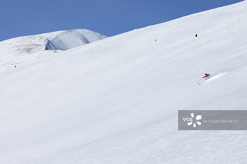 在蓝天白云下，男人在未开发的雪山上滑雪图片素材