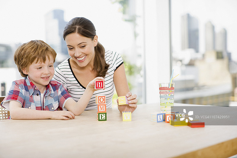 母亲看着儿子堆叠字母积木，拼写单词图片素材