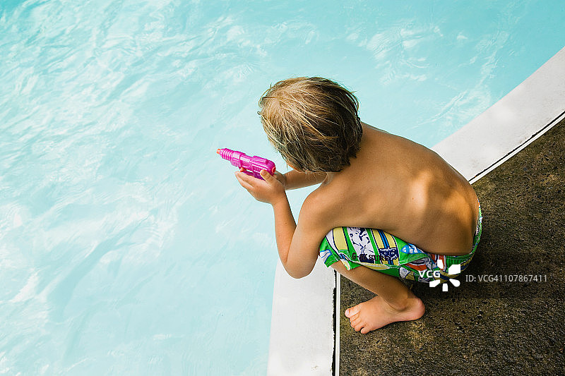 小男孩在泳池边玩水枪图片素材