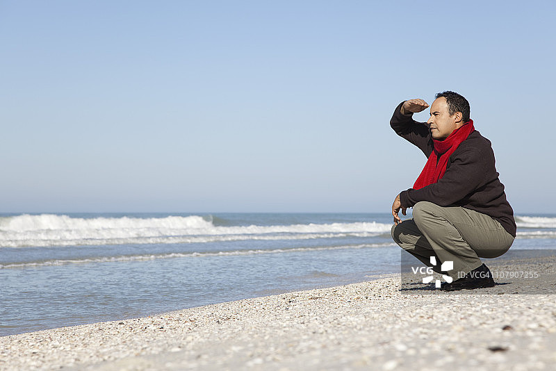 男人蹲在海滩上，看着大海图片素材