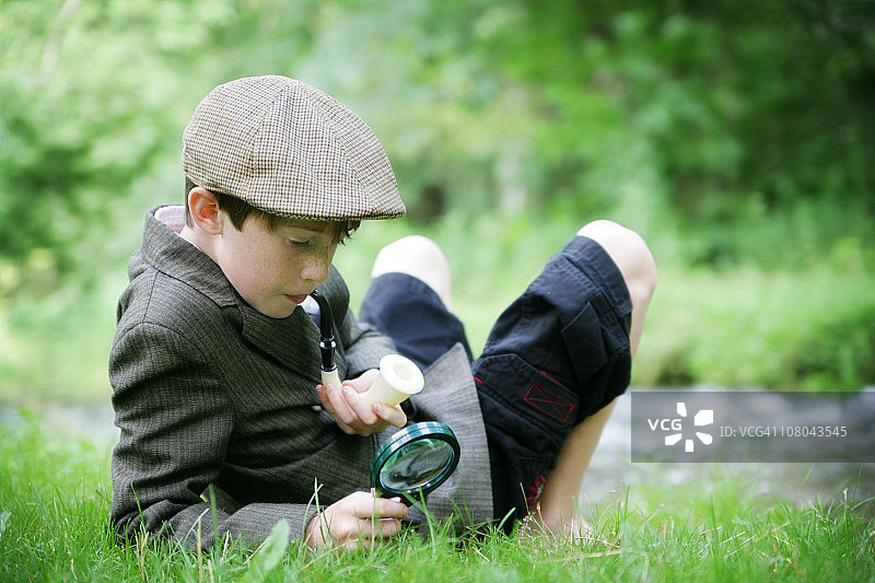 装扮成夏洛克·福尔摩斯的儿童在自然界中使用放大镜图片素材