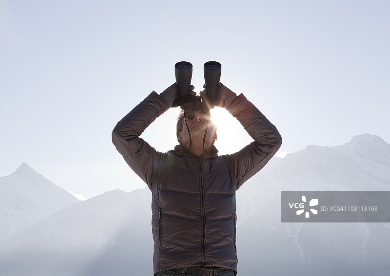 男子用双筒望远镜向上看山脉图片素材