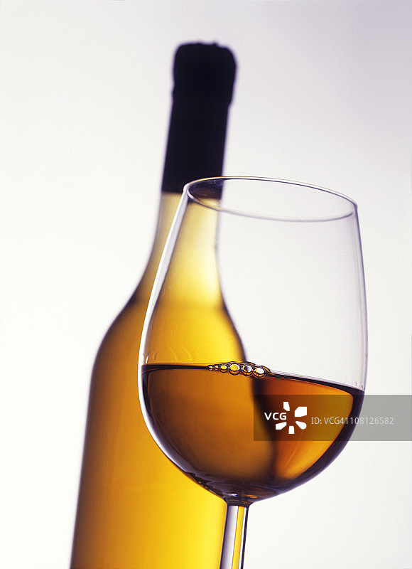 背景为酒瓶的白葡萄酒杯图片素材