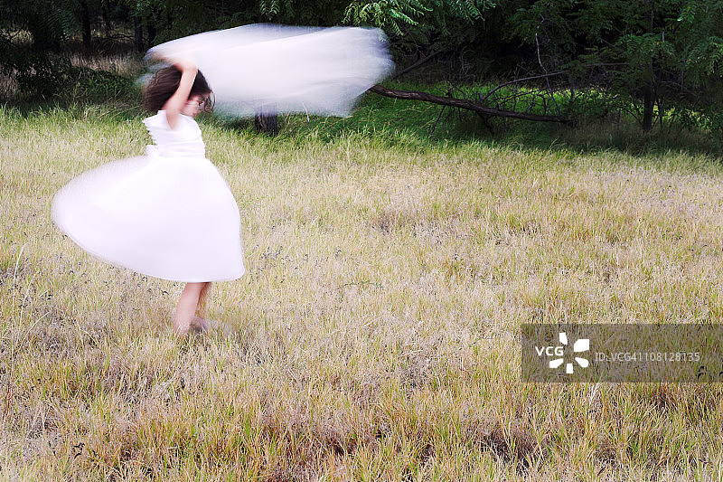 穿着白色连衣裙在田野里旋转的小女孩图片素材