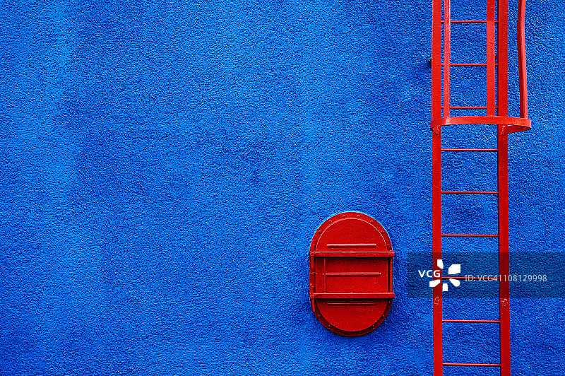 蓝色墙上的红色梯子和活板门图片素材