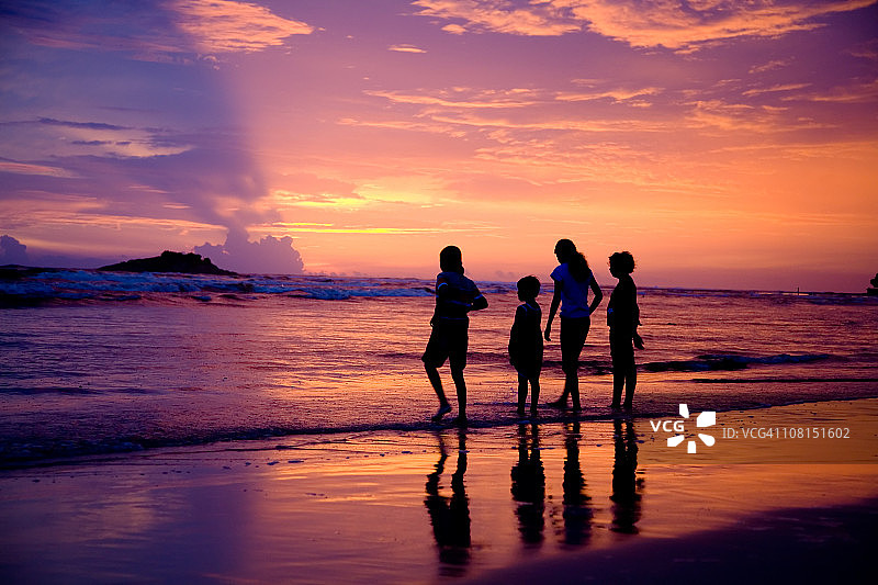 日落时海滩上四个孩子的剪影图片素材