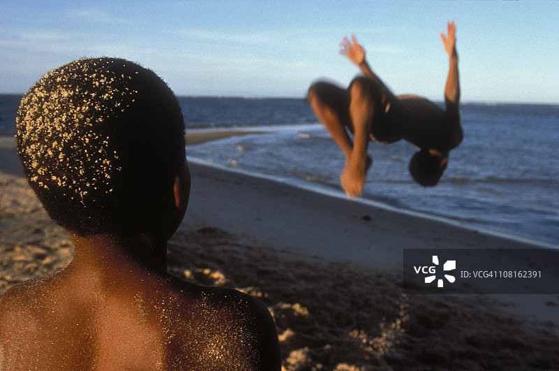 儿童观看男子在海滩上后空翻图片素材