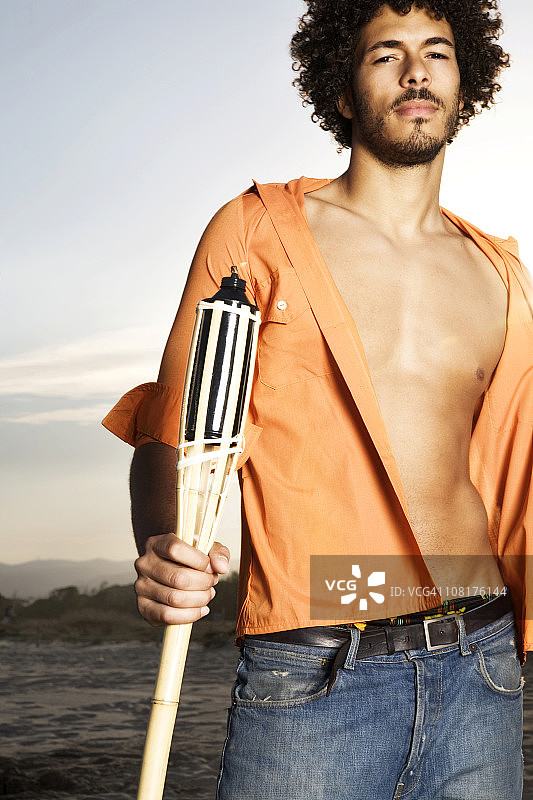 在海滩上拿着火把，敞开衬衫的年轻男人图片素材