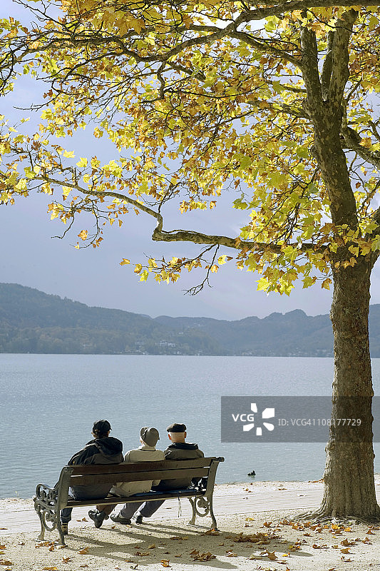 秋天坐在湖边长椅上的一群老年男人图片素材