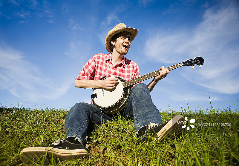 乡村男孩在夏日草甸上弹奏班卓琴图片素材