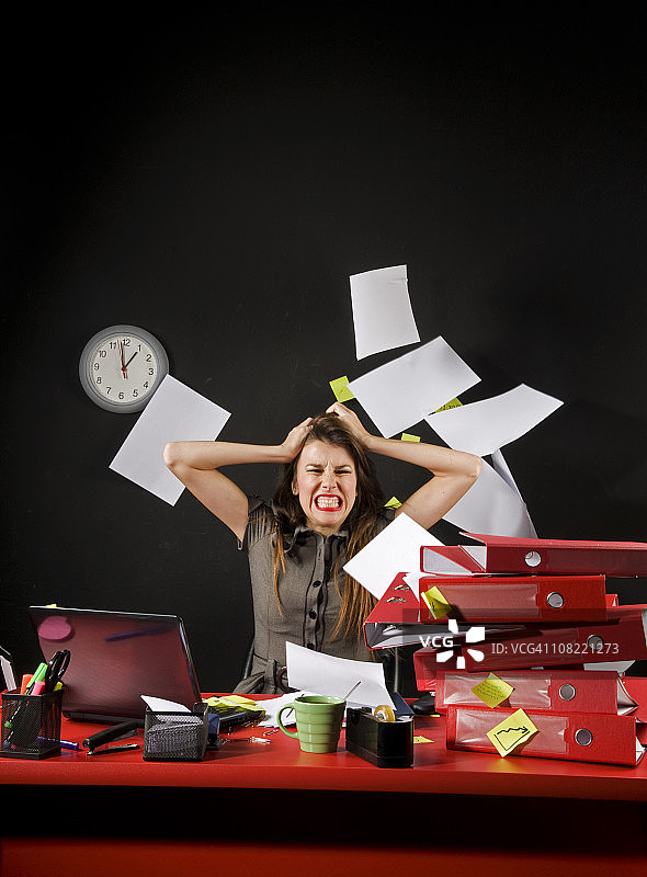 沮丧的女商人坐在凌乱的办公桌旁，纸张乱飞图片素材