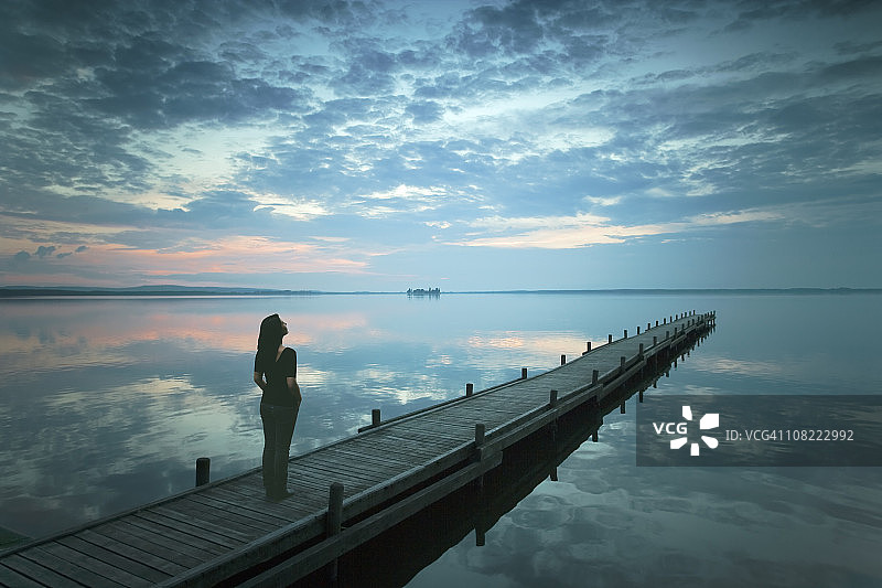 黄昏时分站在湖边码头上的年轻女子轮廓图片素材
