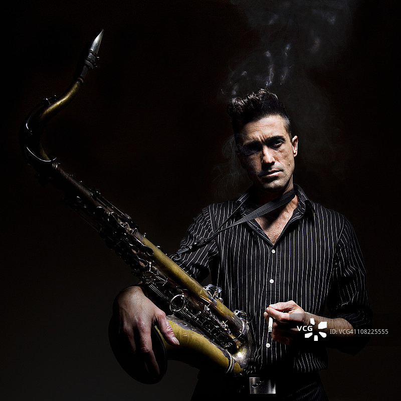 在黑色背景上抽烟并拿着萨克斯的男人图片素材