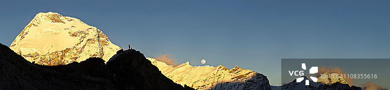 登山者观看日落时金色山顶全景及满月升起图片素材
