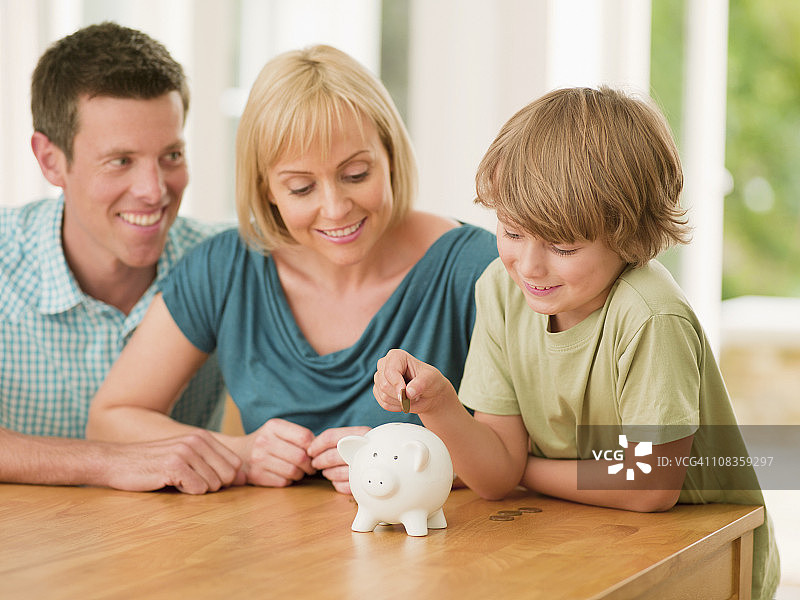 父母看着儿子把硬币放进存钱罐图片素材