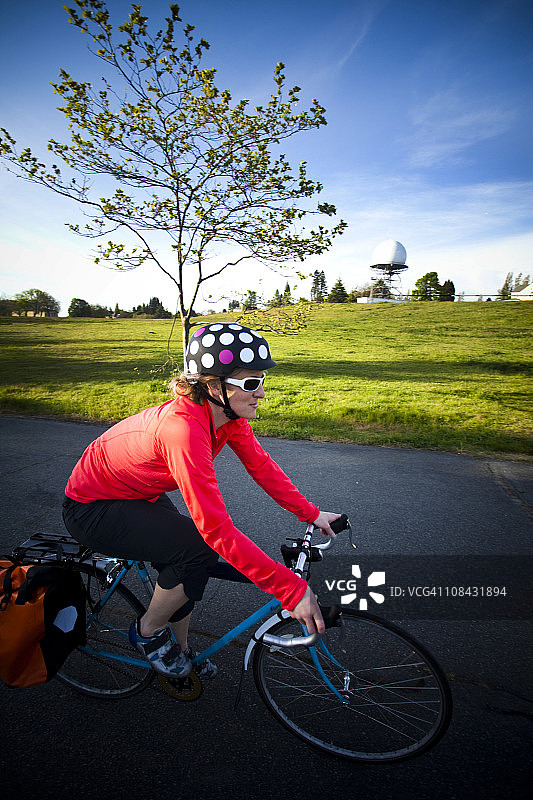 年轻女子在日落时分骑自行车穿过公园图片素材
