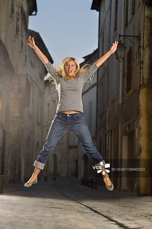 年轻女子在黄昏时分的街道上跳跃图片素材