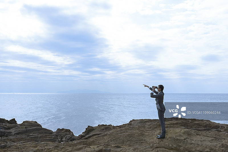 商人在悬崖上用望远镜观察图片素材