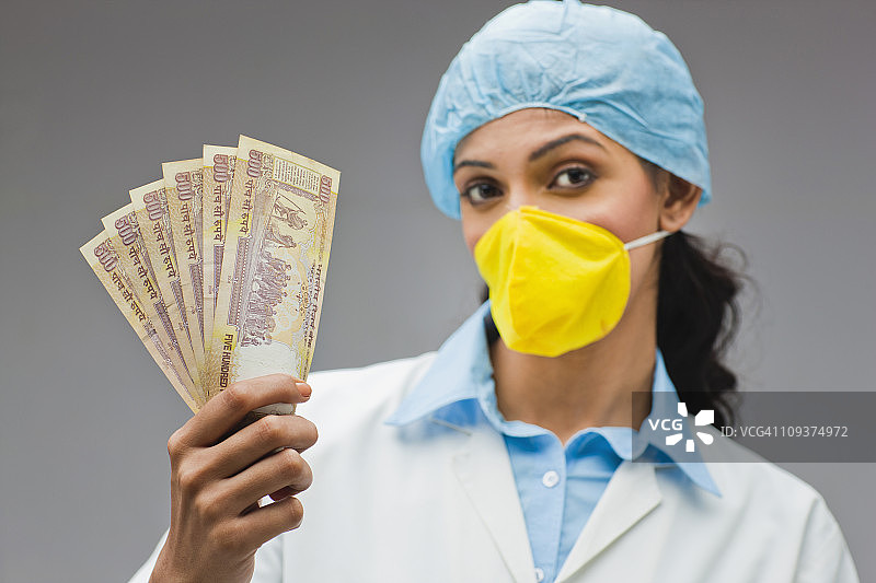 戴着手术帽和口罩的女人拿着扇形展开的钞票图片素材