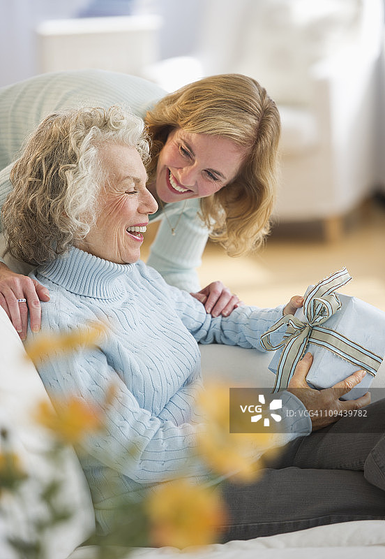 美国新泽西州泽西市，年长的妇女在沙发上收到女儿的礼物图片素材