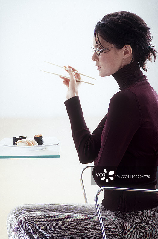 拿着筷子看着寿司盘的女商人图片素材