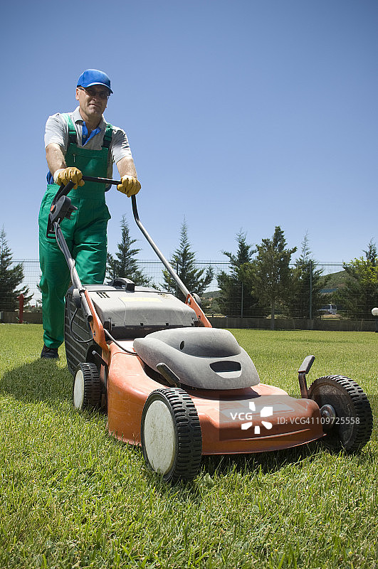 穿工作服的男园丁在推割草机图片素材