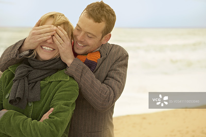 情侣在海滩，男人用手捂住她的眼睛图片素材
