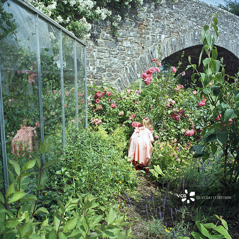 女孩在温室旁的花丛中玩耍图片素材
