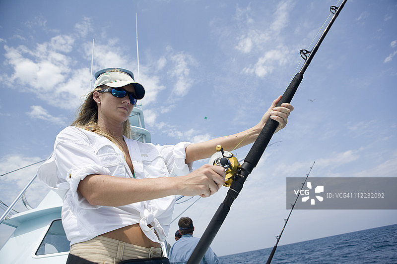 金发女人拿着钓鱼竿，同时观察是否有旗鱼上钩图片素材